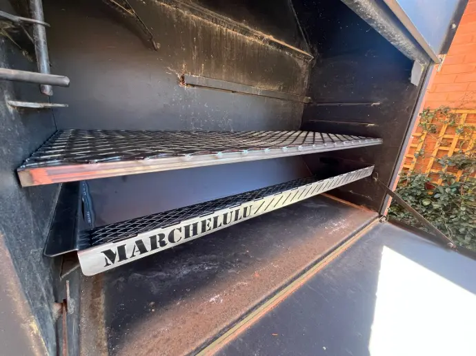 A custom-fit Marchelulu braai grid and coal insert installed perfectly inside a large, black, built-in braai showcasing a made-to-measure solution.