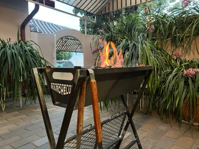 The Marchelulu V-Bucket and stand used as a complete freestanding braai on a patio, showcasing its dual-purpose and portable design.
